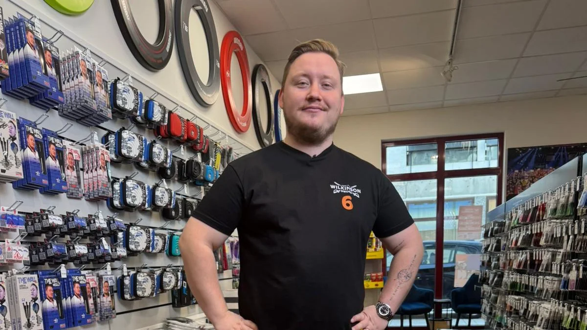 Martin Schindler in einem Darts-Shop vor einer Wand mit seinen The-Wall-Darts